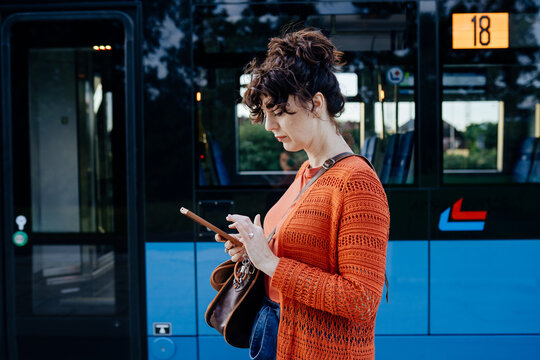 Focused young female commuter using smartphone beside modern city tram
