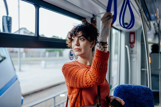 Attentive young woman holding strap inside modern tram during urban commute