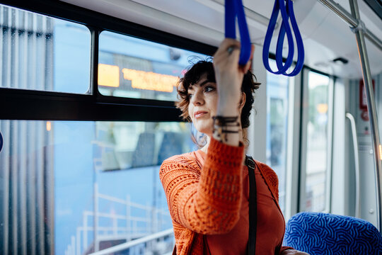 Attentive young female passenger holding strap inside modern public tram