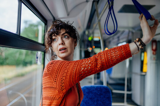 Surprised young woman holding overhead strap while traveling by public tram