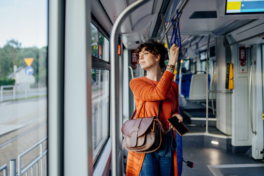Independent female commuter standing with smartphone inside modern city tram