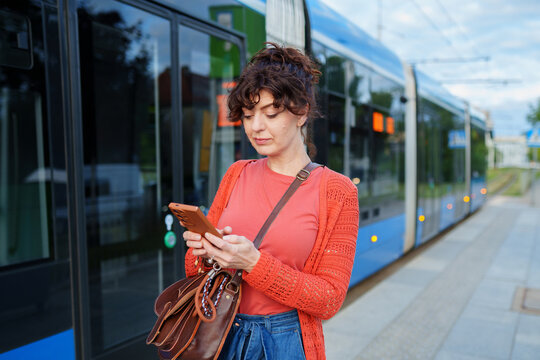 Focused female commuter using smartphone beside modern tram at urban station
