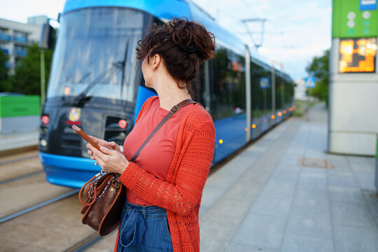 Attentive female commuter watching tram arrive at modern urban transport stop
