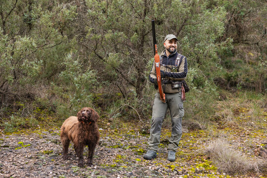 Hunter standing with spanish water dog and shotgun