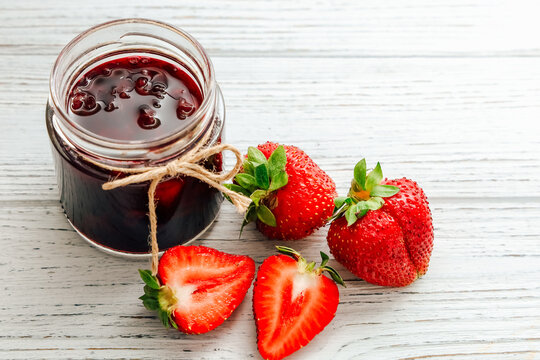 Fresh strawberries and homemade jam on a wooden table in daylight