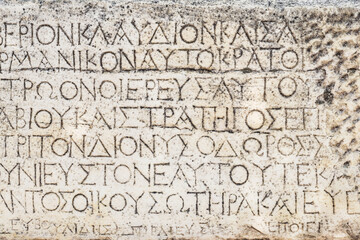 Fototapeta premium Ancient Greek inscription carved in weathered stone. A close view of carved Greek letters on a rough weathered stone surface.