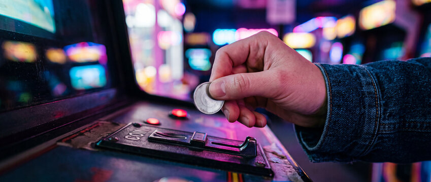 Player inserting coin into retro arcade machine with neon lights and gaming controls