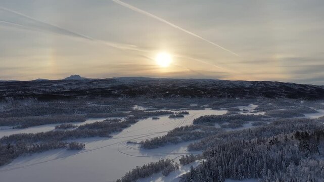 Aerial view of sun halo over snowy forest and frozen lake, Norway
