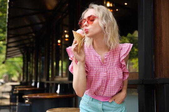 Beautiful woman in sunglasses posing with waffle cone with delicious ice cream at outdoor cafe. Space for text