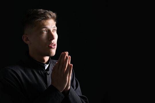 Priest with clasped hands praying on black background. Space for text