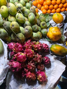 Fresh colorful assortment of tropical fruits including mangoes dragon fruits papaya and oranges displayed at a local outdoor market stall on white wrapping paper for sale to customers.