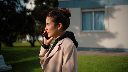 Side profile of a young Latina woman walking on the street while talking on the phone, representing communication, urban lifestyle, and modern daily life. © Emanuel