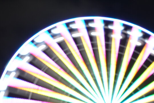 Blurred Night Lights of a Vibrant Amusement Park with Ferris Wheels and Carnival Rides.