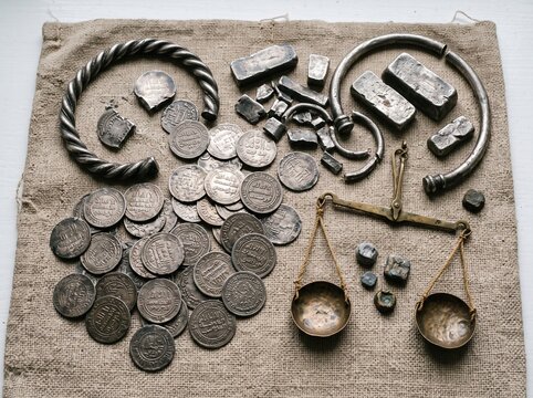 A collection of ancient silver coins, ingots, and a weighing scale, suggesting a historical display of wealth and trade