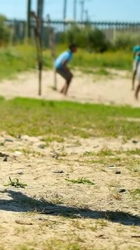 Vertical video: Stepping off peg, barefoot teen green-top kicking ball to play on sand, copy space