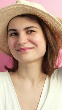 Vertical video of young beautiful happy brunette woman in straw hat smiling on the pink background