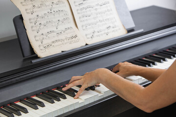 Woman playing digital piano while reading vintage sheet music during music practice. Close-up of female hands playing a digital piano with aged sheet music on the music stand.  © NataSao