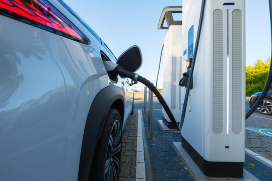 Electric car charging at a outdoor public charging station. Close up of EV charger cable connected to modern electric vehicle.