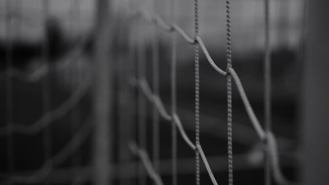 Cinematic black and white close-up of a soccer goal net with shallow depth of field. Monochrome sports background featuring texture, geometry, competition, and football concepts.

