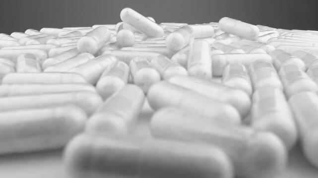 Numerous white capsules are arranged in a random pattern, representing medicine, supplements, and wellness trends. The monochrome palette emphasizes cleanliness and scientific advancement