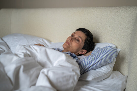 Unhappy thoughtful senior woman lying in bed in morning at home with lost exhausted expression, elderly female in bedroom showing loneliness and depression at older age, life after divorce. Melancholy