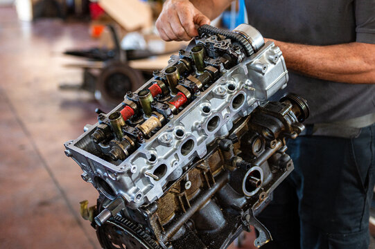 Close-up of a professional auto mechanic inspecting the timing chain, camshaft and valve train on a rebuilt four-cylinder engine during repair and maintenance in an automotive workshop.