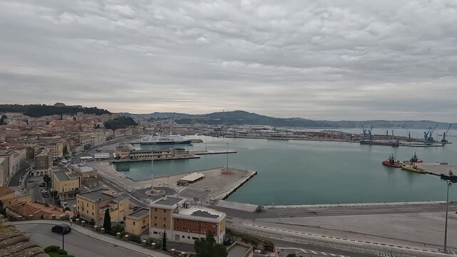 Ancona, Marche, Italy. Slow panoramic camera pan from Guasco Hill across Santi Pellegrino e Teresa Church, historic city rooftops and the Adriatic port under a hazy spring sky.