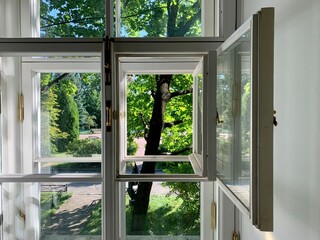 Obraz premium Open white wooden window with view of green sunny garden park and trees. Bright summer day interior background concept. 