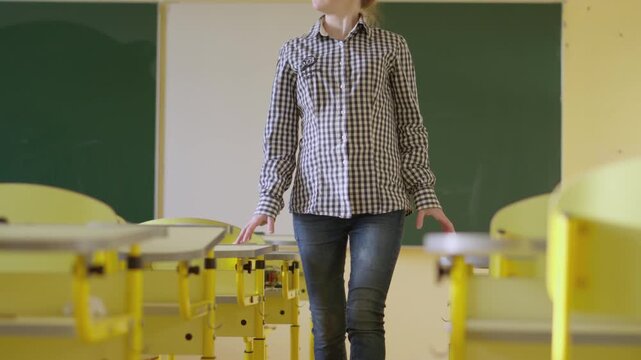 A pregnant woman is seen standing in a bright, empty classroom, surrounded by yellow desks and a green chalkboard. The scene highlights maternity in a contemporary educational setting