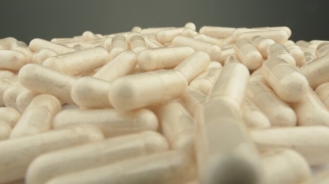 Numerous white capsules are arranged in a heap, representing dietary supplements or medication. The photo captures the growing popularity of wellness products and the pharmaceutical industry