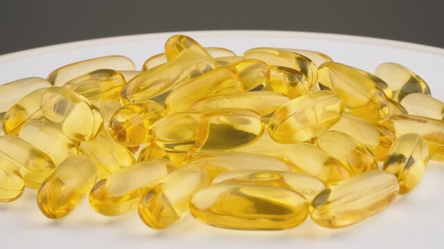 Features pile golden softgel capsules, often associated with vitamins or dietary supplements, displayed in clean, clinical setting. Focus is on clarity, shine each capsule