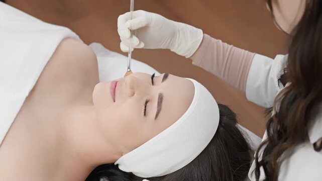 Serene female client enjoys rejuvenating facial mask application by expert esthetician in contemporary wellness clinic. Soothing spa procedure promotes healthy, glowing skin, relaxation