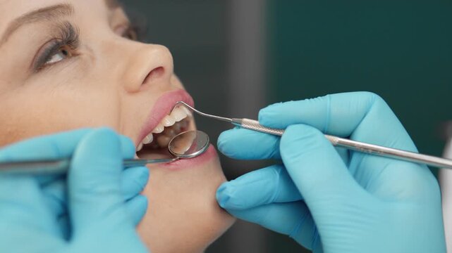 Dentist in blue gloves carefully examines patient's teeth using dental instruments during routine checkup. Oral health, prevention, professional care are highlighted in this modern dental clinic