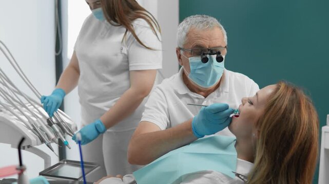 Professional dental team provides oral care in a bright, contemporary dental office. Dentist focuses on patient&rsquo;s teeth while assistant supports the procedure, ensuring a safe and sterile environment