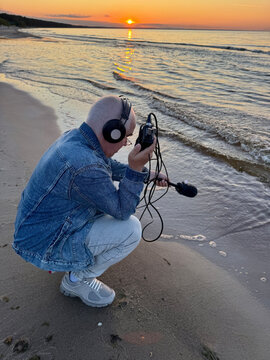 Sound Recordist Recording Ocean Waves at Sunset on Sandy Beach