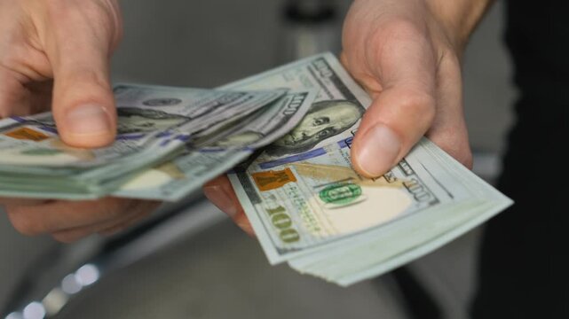 A person counts a stack of hundred dollar bills, emphasizing the importance of money management and financial planning. This photo represents savings, income, and modern business finance