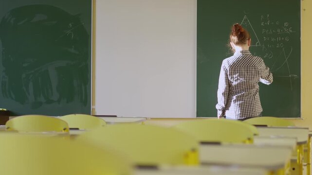 A woman educator stands at the blackboard, illustrating a triangle and equations during a math lesson in a bright, modern classroom. The scene captures a moment of preparation before students arrive