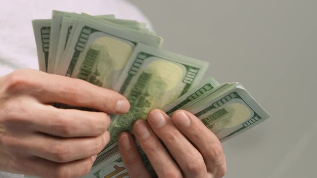 A person is carefully counting a thick bundle of hundred dollar bills, representing income, savings, and economic growth. This photo highlights themes of finance, investment, and abundance