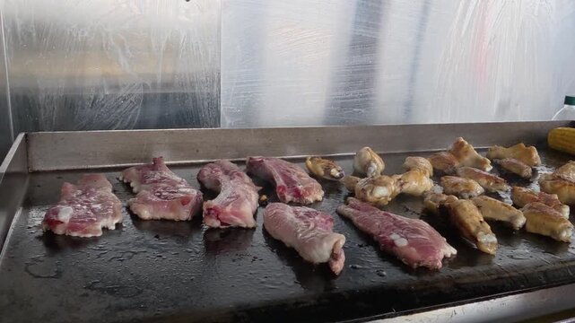 Chef cooking meat pork ribs and chicken wings on a griddle