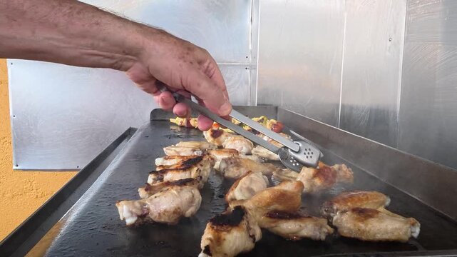Chef cooking chicken wings and vegetable skewers on griddle