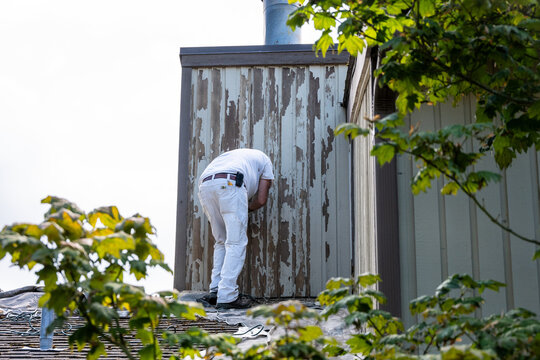 Professional house painter preparing an exterior wall of residential home for new paint job, scraping and sanding off old paint, to preserve old wood siding, maintenance and upkeep
