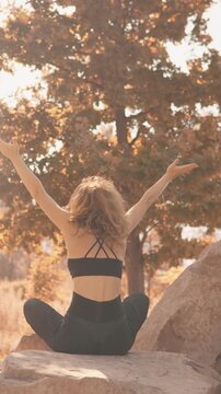 Young woman in activewear meditates in a peaceful autumn landscape, surrounded by trees and soft sunlight. Tranquil outdoor yoga session promotes mindfulness and relaxation
