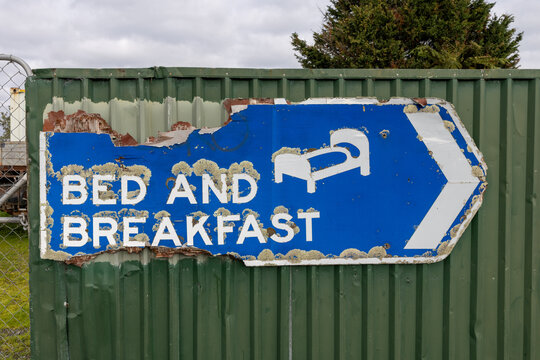 A weathered and peeling Bed and Breakfast sign attached to a green metal fence in rural Shannon, New Zealand, pointing travelers toward lodging.