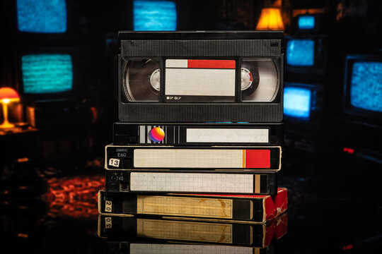 Stack of vintage VHS cassette tapes against blurry retro TVs back
