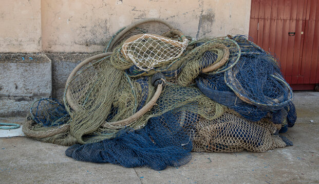 Large pile of blue and green commercial fishing nets with floaters on concrete ground at harbor quay