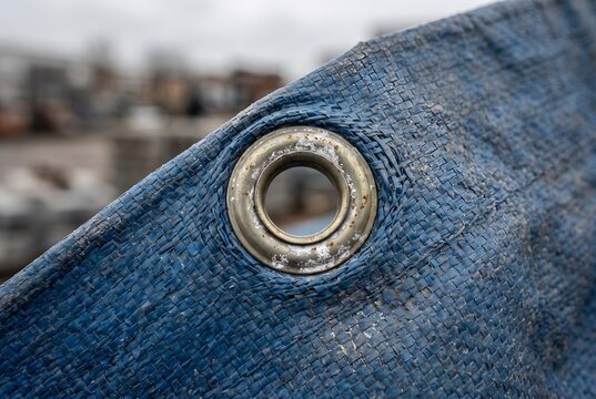 Macro close up of a metal grommet eyelet on a blue tarp showing strained fabric and faint oxidation