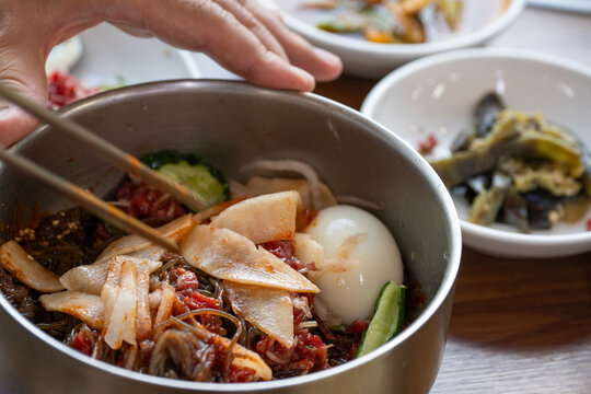 Traditional Korean yukhoe bibimbap being mixed in a traditional brass bowl.