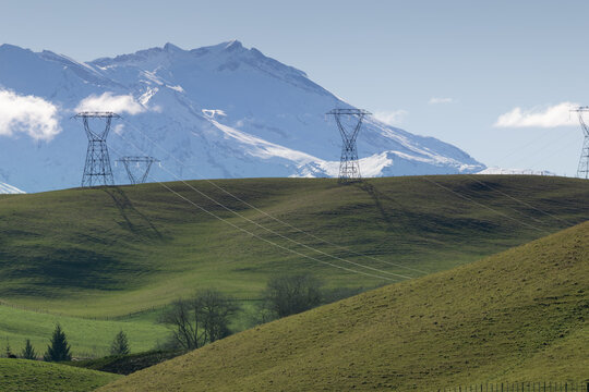 View of the snow-capped Mount Ruapehu peak rising above the rolling green pastoral hills of the Ruapehu District, New Zealand.