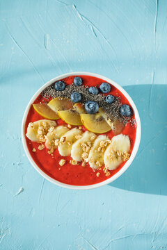 healthy smoothie bowl with granola, banana and fresh blueberries on color background