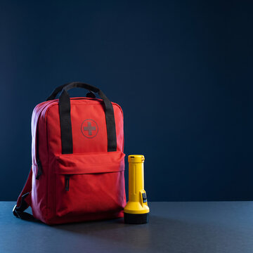 Red emergency backpack and yellow flashlight in a dramatic blue studio